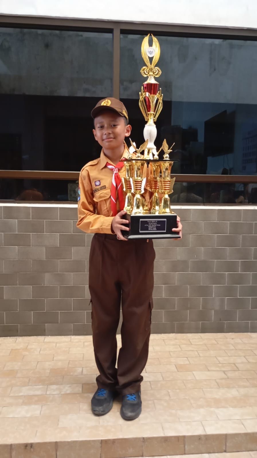 Azka berseragam pramuka memegang piala besar Juara 1 Regu Penggalang